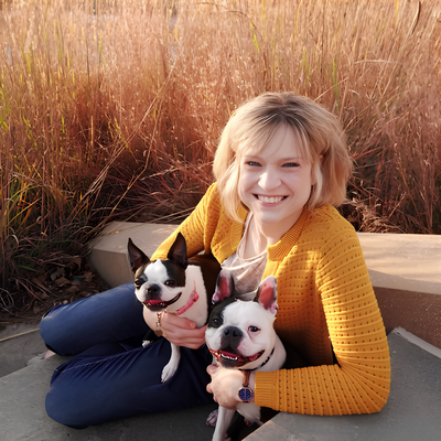 Woman smiling outdoors with two Boston terriers.