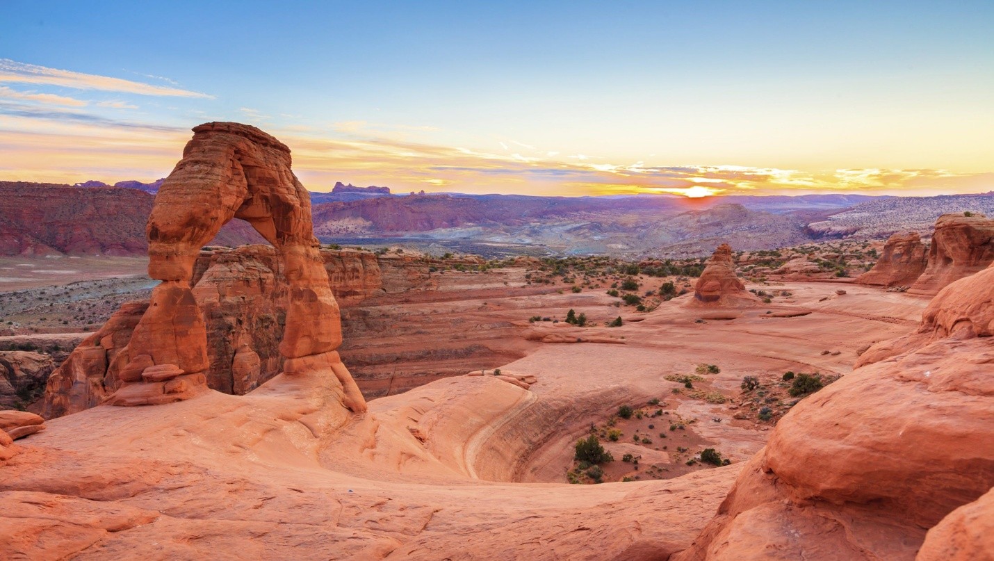 Delicate Arch at sunrise overlooking Utah's red rock desert beneath a colorful morning sky.