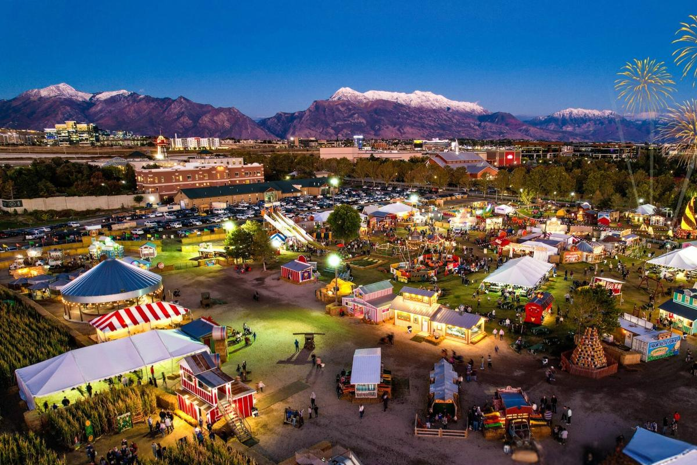 Salt Lake City fairgrounds at dusk with carnival rides, tents, and the Wasatch Mountains in the background.
