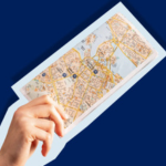 Hand holding a city map against a dark blue background.
