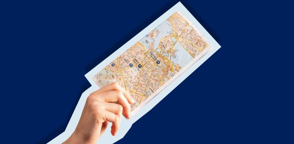Hand holding a city map against a dark blue background.