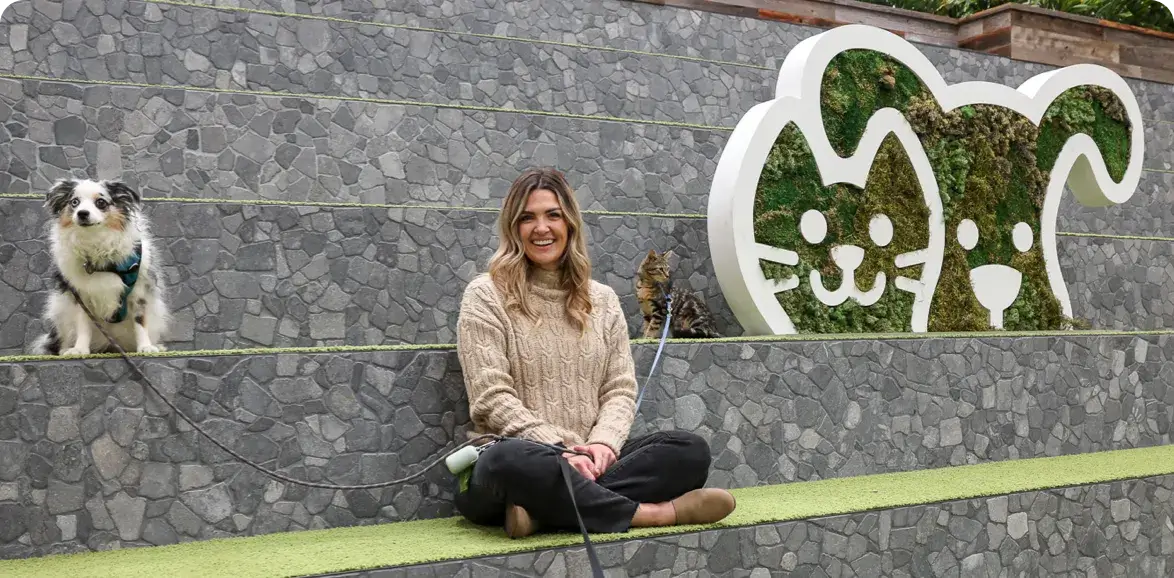 A woman with leashed dogs sits next to a Petco sign