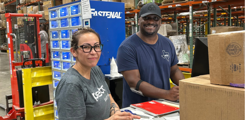 Three employees stand next to boxes in a warehouse