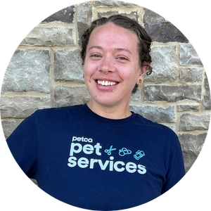 Smiling Petco Pet Services partner standing in front of a stone wall.