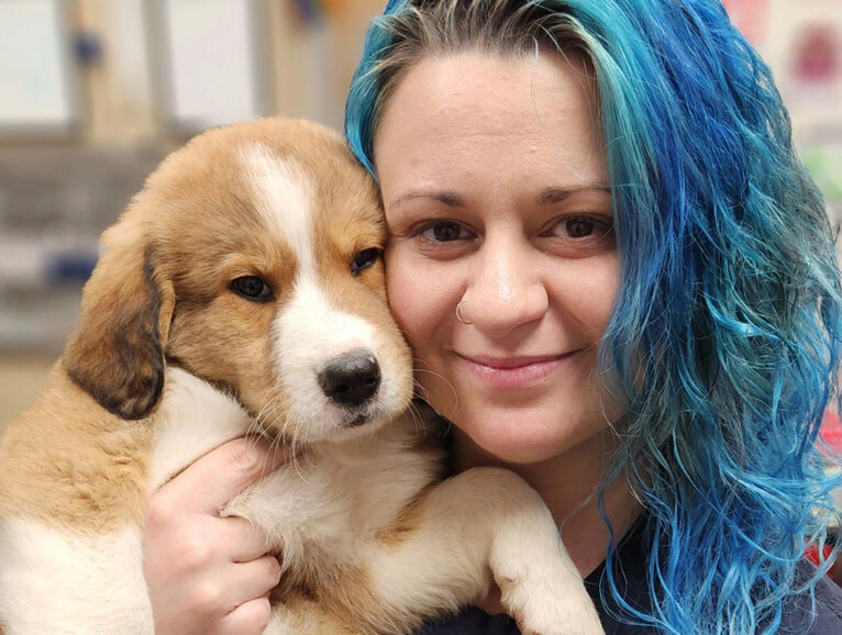 Woman with colorful hair snuggling a puppy close to her body and face