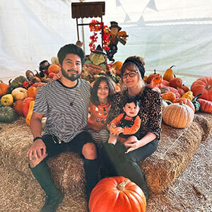 Jovanny sitting on hay with his family posing for a picture and surrounded by pumpkins