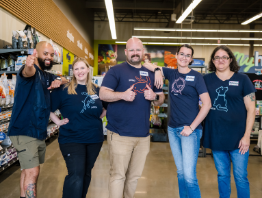 Five Petco partners smiling together inside a pet care store.