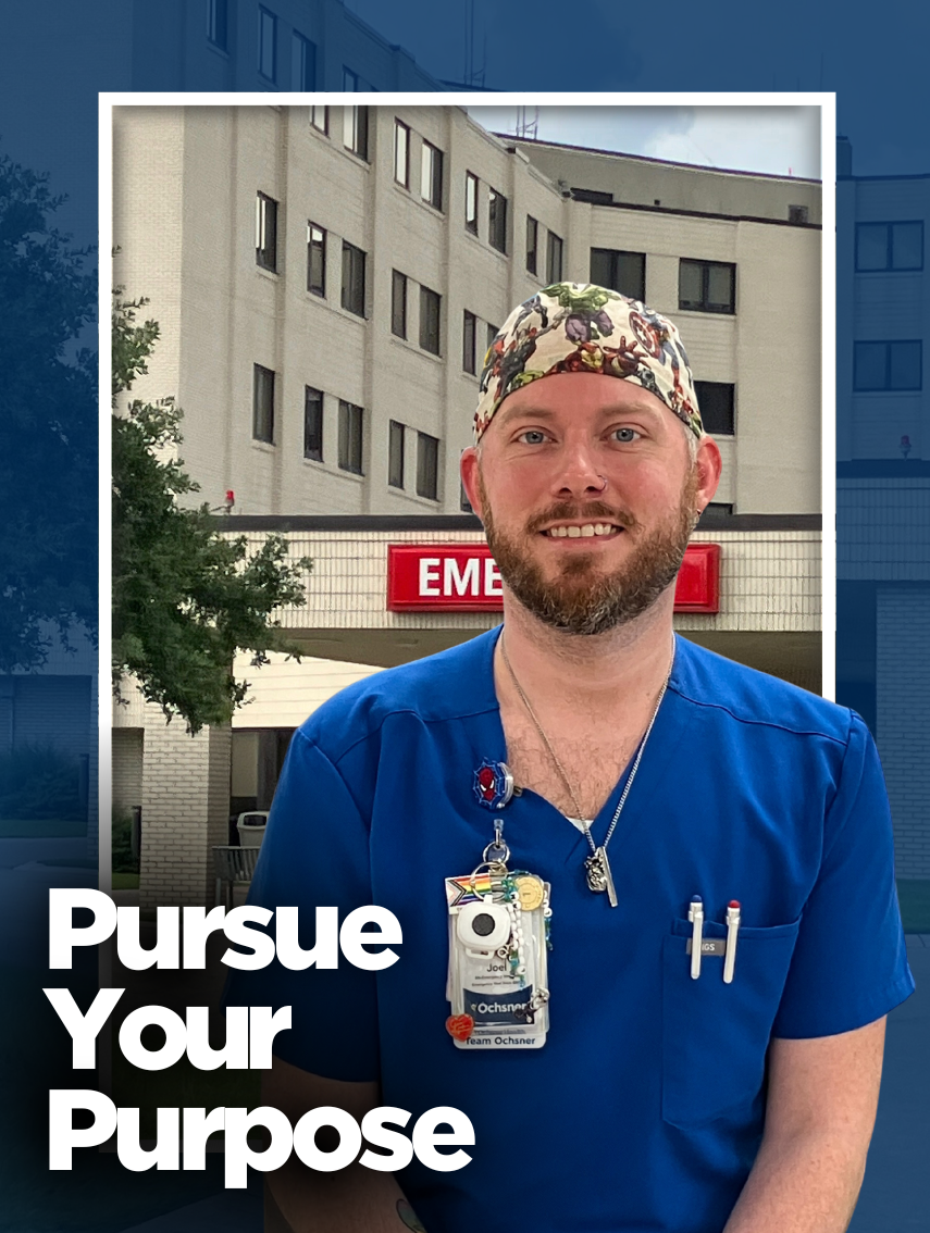 Joel, a smiling male healthcare professional with a reddish-brown beard, wearing bright blue scrubs and a colorful scrub cap, stands in front of the Emergency Room at Ochsner Baton Rouge.