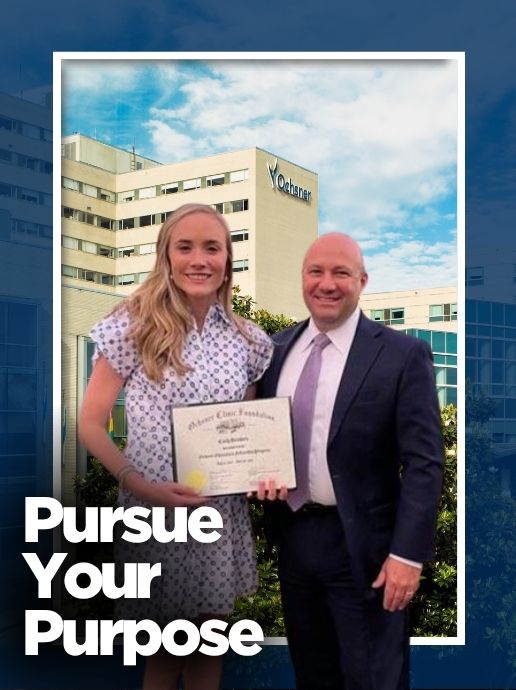 A young woman in a patterned white dress holds a scholarship certificate while standing next to an older man in a suit with a city skyline in the background.