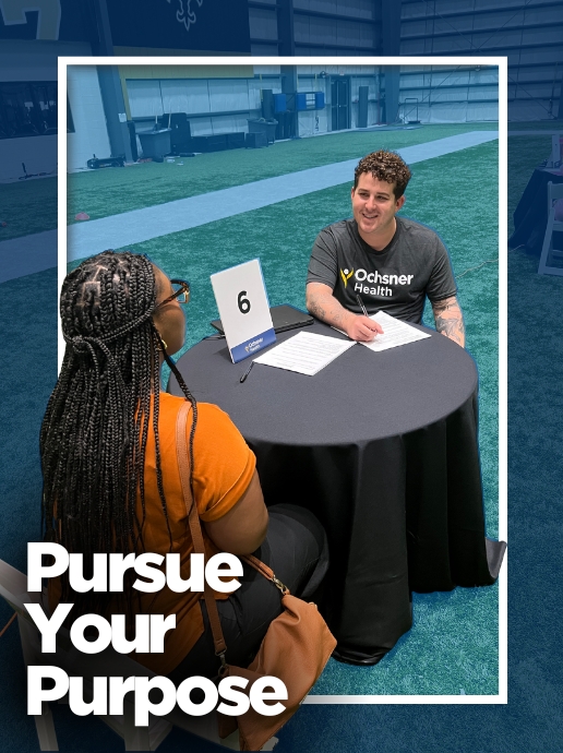 Two people sit across from each other at a round table inside an indoor sports facility, reviewing paperwork next to a sign marked "6." Text reads, "Pursue Your Purpose."