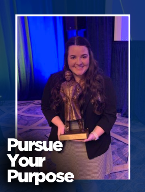 Smiling woman with long dark hair holds a bronze trophy, standing against a backdrop of dark curtains and blue-green stage lighting. The text 'Pursue Your Purpose' overlays the bottom left corner.