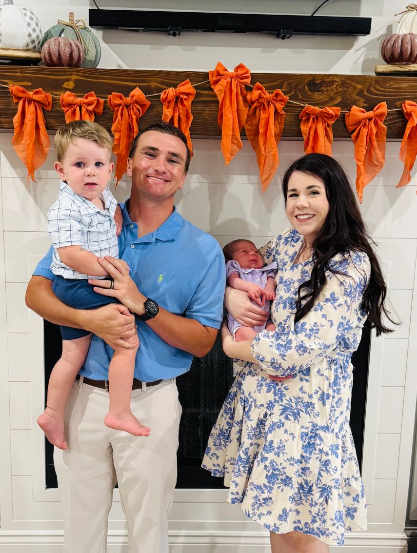Dark haired women holding baby standing next to a male in a blue shirt holding a toddler. 