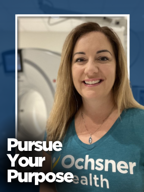 A smiling women in a teal colored Ochsner Health T shirt in front of a CT machine.