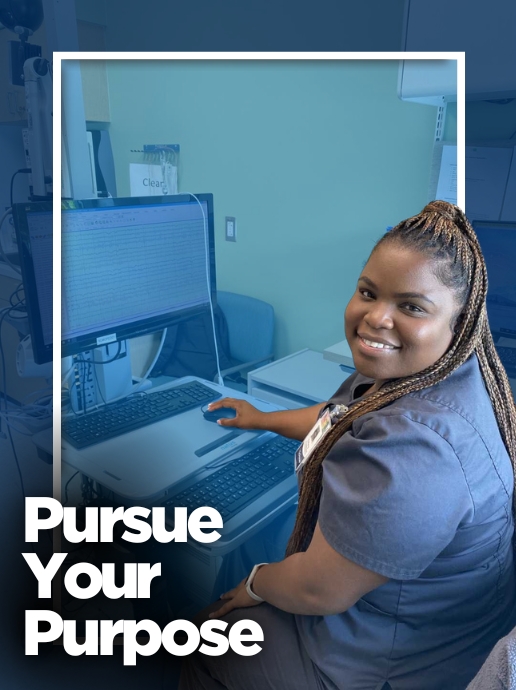 A woman in grey medical scrubs sits at a computer workstation inside a clinical room. Text reads, "Pursue Your Purpose."