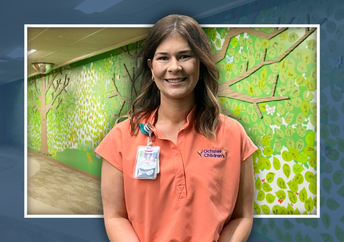 A smiling female nurse in peach scrubs stands in front of a decorative wall featuring green leaf-shaped cutouts with names and footprints.