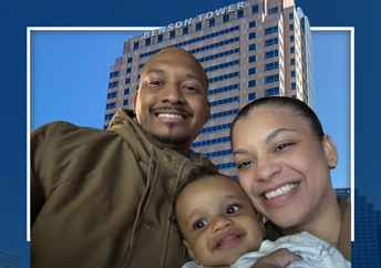 Close-up selfie of a family of three, smiling in front of a blue-toned image of Benson Tower, framed by a white geometric border.
