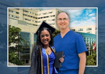 A man and a woman stand in front of a hospital building; the woman wears a graduation cap and gown and holds a diploma, and the man wears blue medical scrubs.