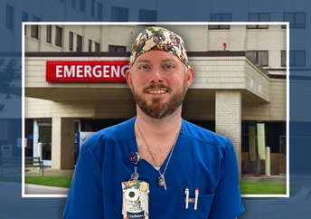 Joel, a smiling male healthcare professional with a reddish-brown beard, wearing bright blue scrubs and a colorful scrub cap, stands in front of the Emergency Room at Ochsner Baton Rouge.