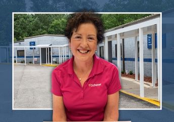 A woman wearing a pink Ochsner polo shirt sits outdoors in front of a clinic building with a covered walkway.