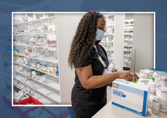 Female pharmacy technician wearing black scrubs and a face mask prepares medications.