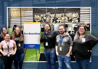 Six people stand together inside an indoor sports facility next to a sign that reads "Pre-Boarding.’”