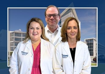 Three doctors, one man and two women, stand smiling in white coats in front the new Patrick Neuroscience Institute building