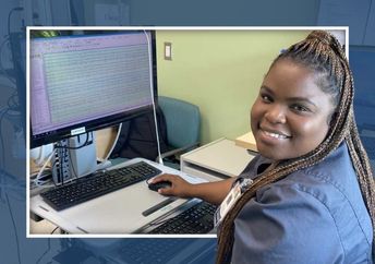 Female tech in grey scrubs sitting at a computer smiling