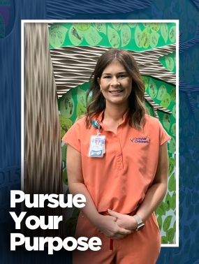 A smiling female nurse in peach scrubs stands in front of a decorative wall featuring green leaf-shaped cutouts with names and footprints.