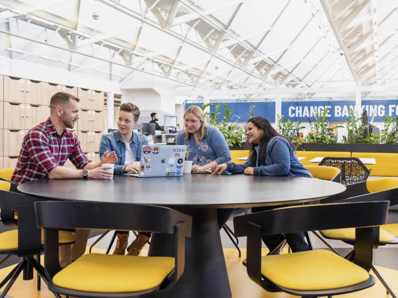 Team chatting around a table in a bright office.