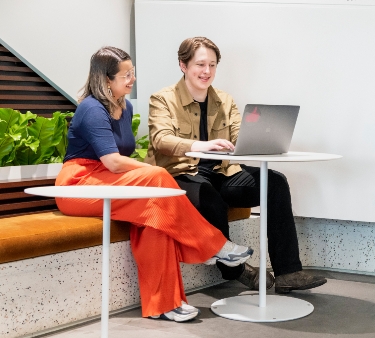 Two people sitting and working on a laptop together.