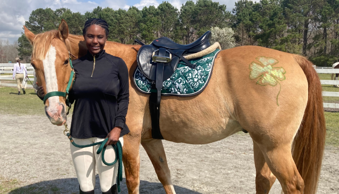 Woman stands in front of a horse that is wearing a saddle