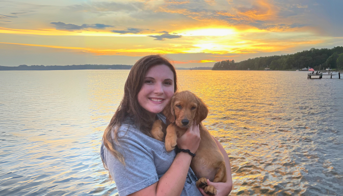 Woman stands with puppy posing in front of large body of water