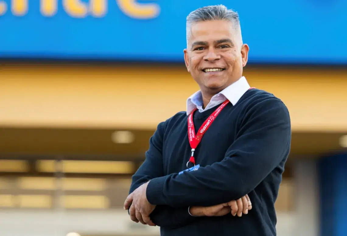 A male Store Manager standing outside of a Walmart while crossing his arms and smiling for a picture