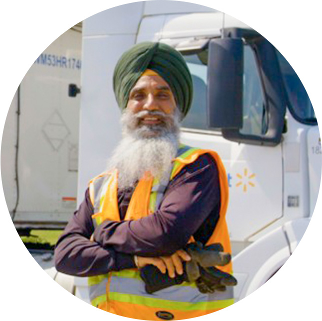 An older man smiling with a long gray beard, turban on his head, and orange safety vest