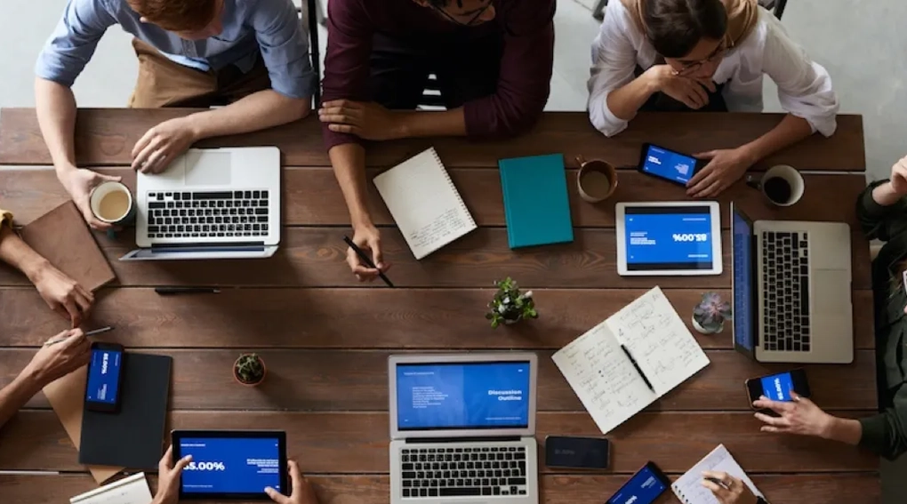 Top-down view of people using laptops and tablets at a table.