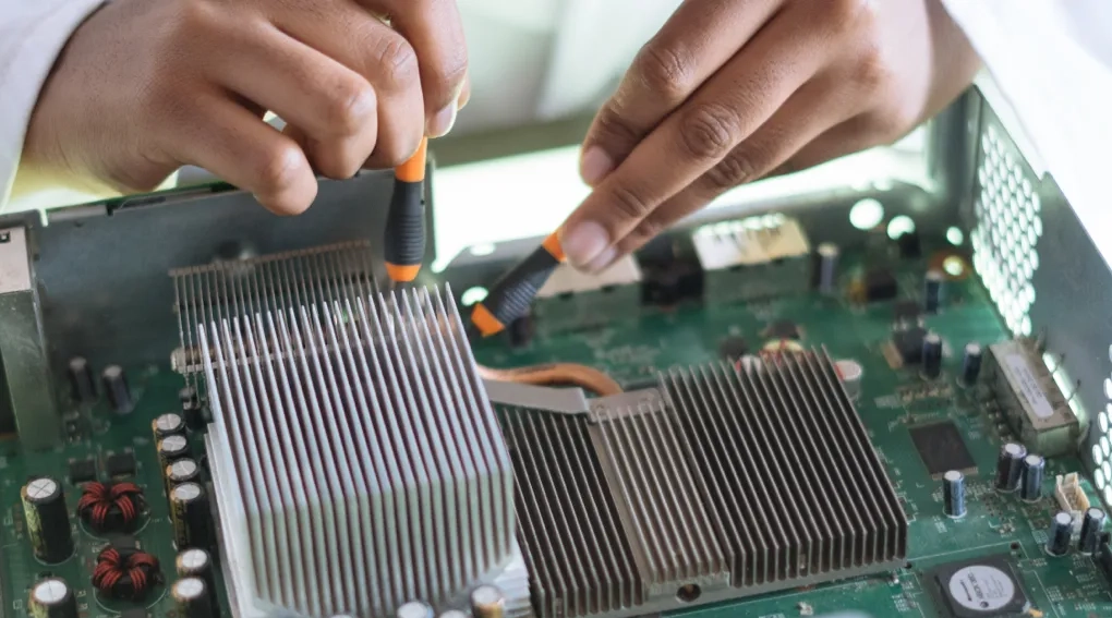 Hands working on a computer motherboard with tools