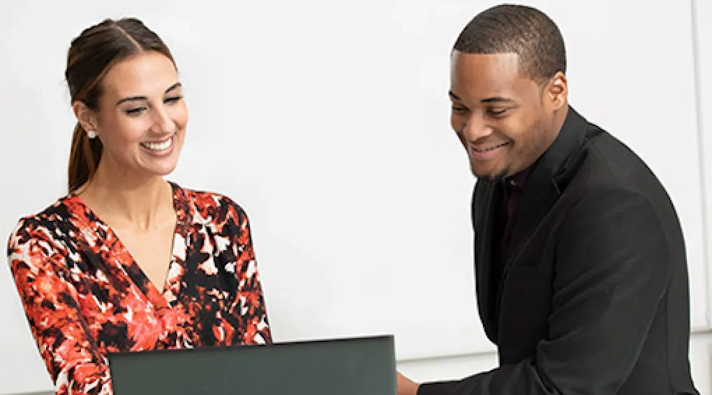 Two young professionals smiling at a laptop