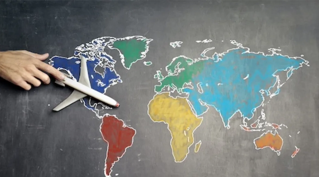 Hand pointing to a world map on a chalkboard.