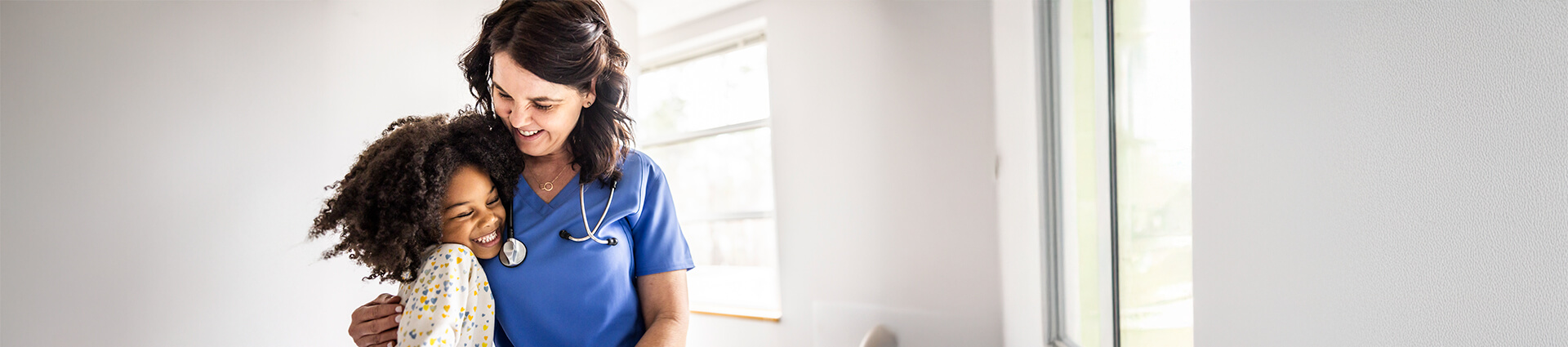 Smiling healthcare worker in blue scrubs with stethoscope hugging a young child