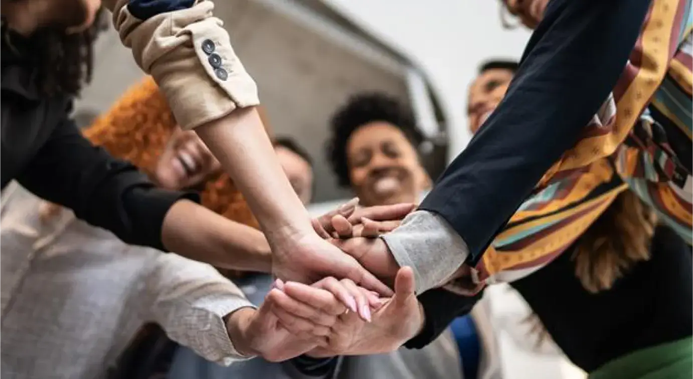 A group of people huddling up and putting there hands atop of one another.