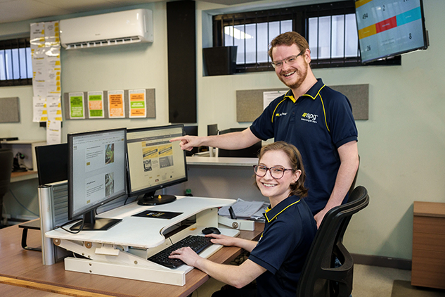 Two workers operating in a packing or distribution area, surrounded by boxes and equipment, symbolizing workplace benefits and support.