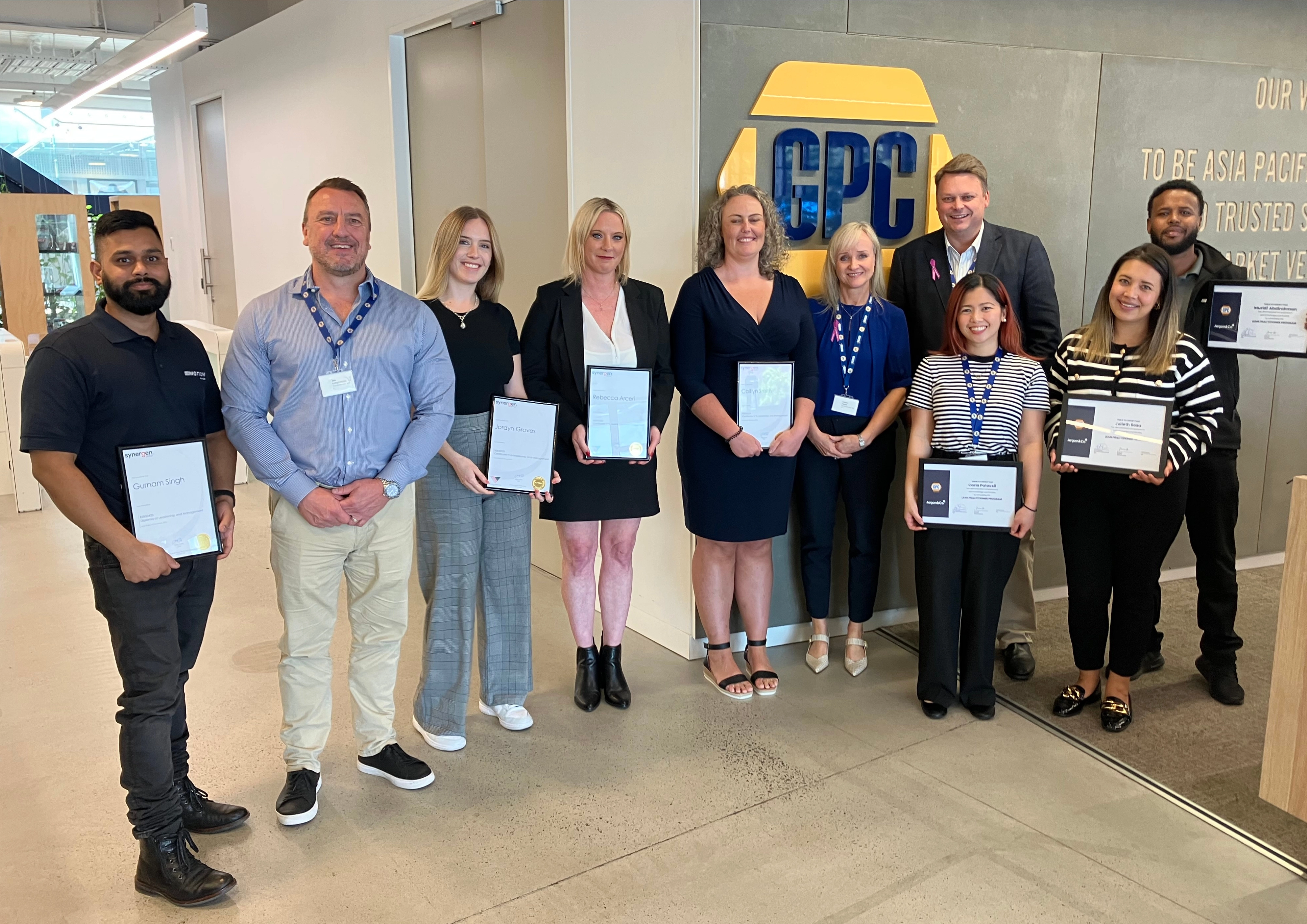 Employees posing indoors with certificates