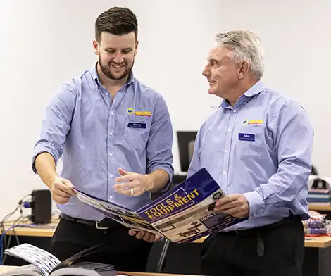 Two men review documents at a table in a store or office
