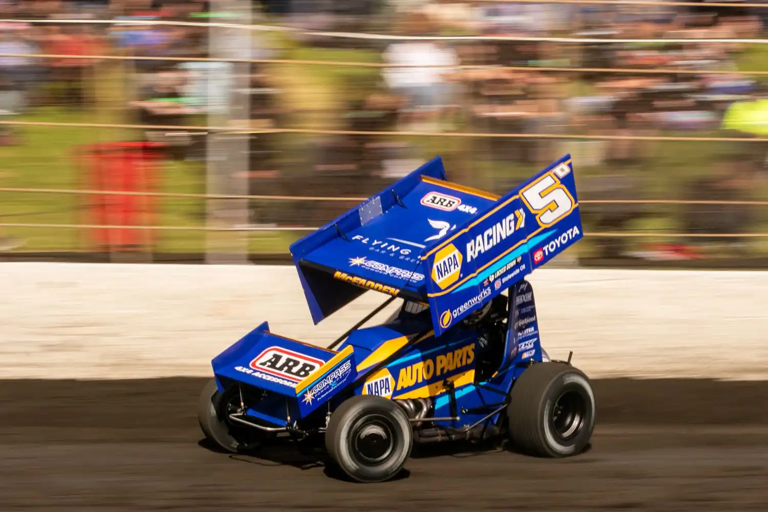 A blue sprint car speeds on a dirt track