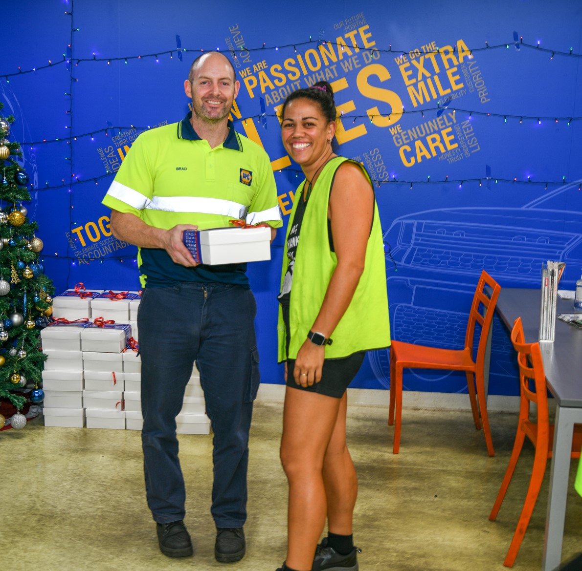Two people in safety vests exchange documents in a warehouse.