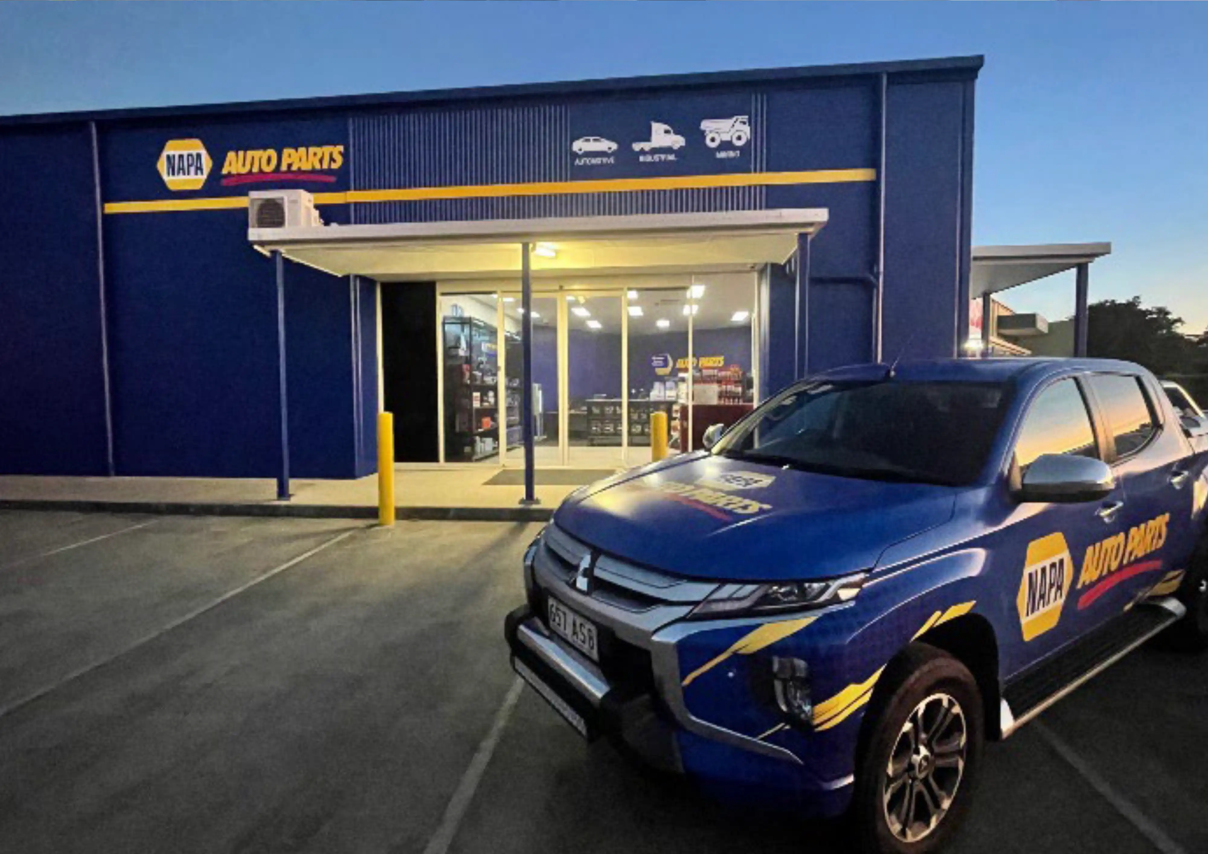 NAPA employees in blue uniforms pose with a branded race car outside.