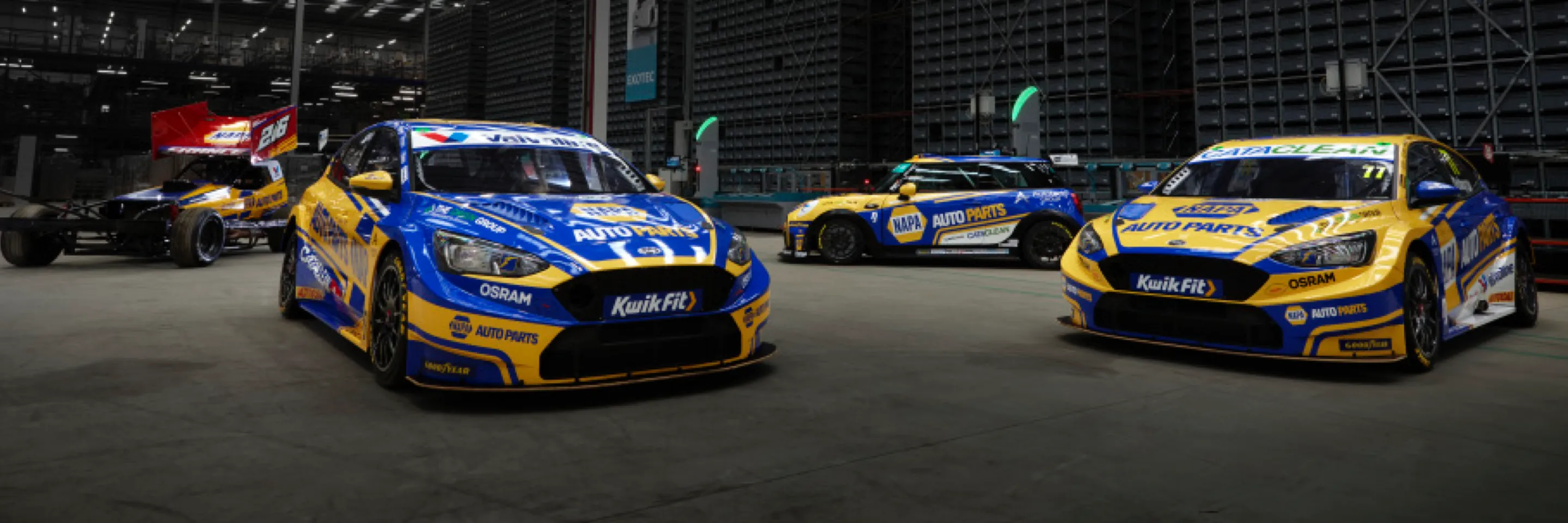 three blue-and-yellow race cars parked on a track at night.