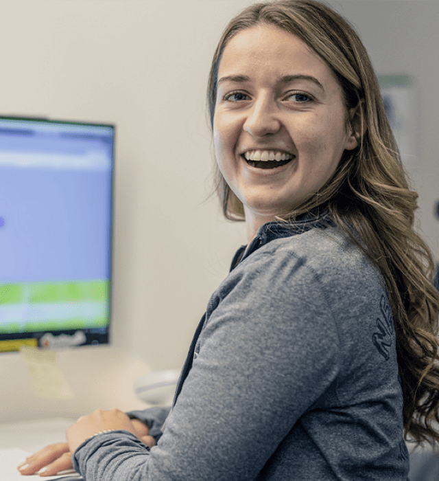 Woman smiling while sitting in front of computer monitor.