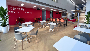 Common area with tables and chairs with sign on the wall reading Skylight Space