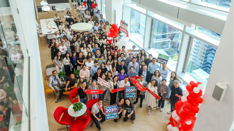 Group photo of Shanghai office team in lobby and on stairs holding signs welcoming to new SCJ office